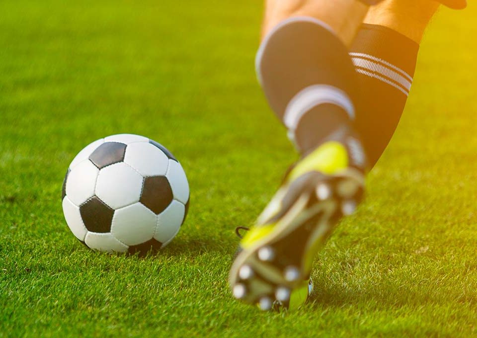 Fußballer mit schwarz-weißen Stutzen holt auf grünem Rasen mit dem linken Bein zu einem Schuss auf den vor ihm liegenden Ball aus.