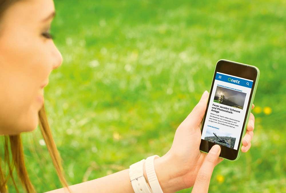 Frau auf Wiese mit Smartphone in der Hand, auf dem das Onlineportal „Onetz“ von Oberpfalz Medien zu sehen ist.