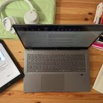 Ein Laptop steht auf einem Tisch, daneben liegen viele Bücher.