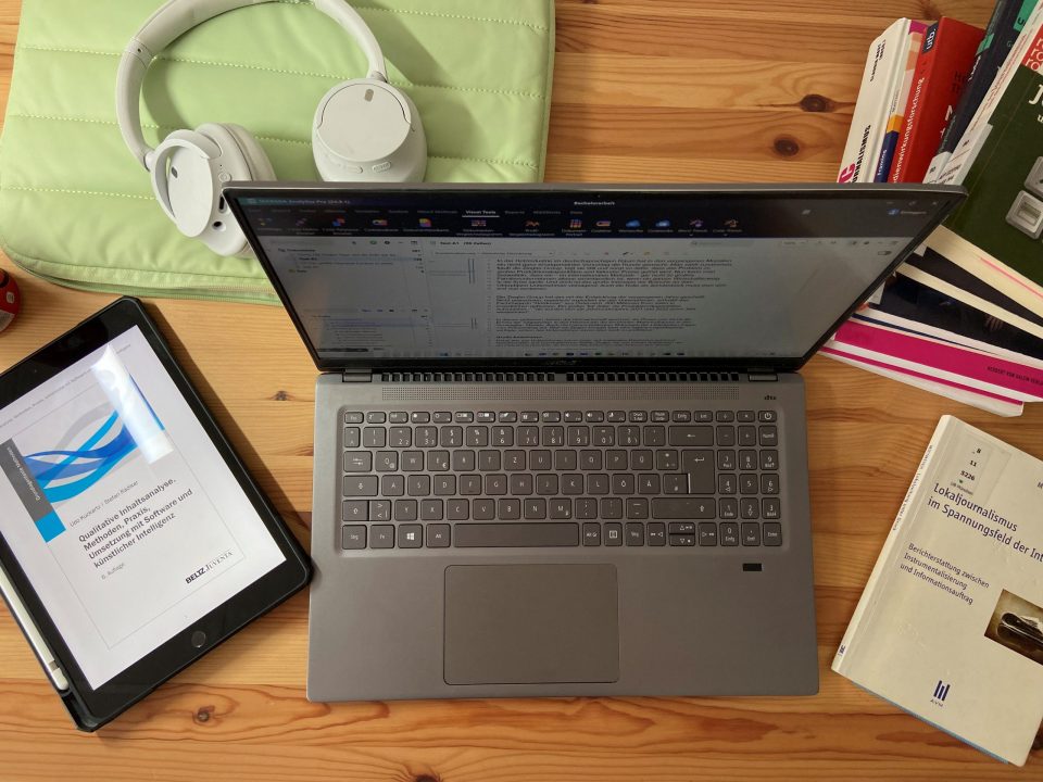 Ein Laptop steht auf einem Tisch, daneben liegen viele Bücher.